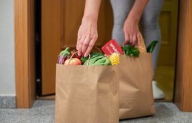 A woman picks up a bag of food at the door of her house. Coronavirus. Quarantine. Stay at home, Online shopping. Vegetables and fruits delivery during quarantine and self-isolation
