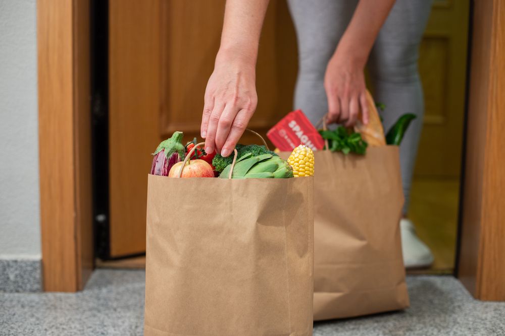 A woman picks up a bag of food at the door of her house. Coronavirus. Quarantine. Stay at home, Online shopping. Vegetables and fruits delivery during quarantine and self-isolation.
